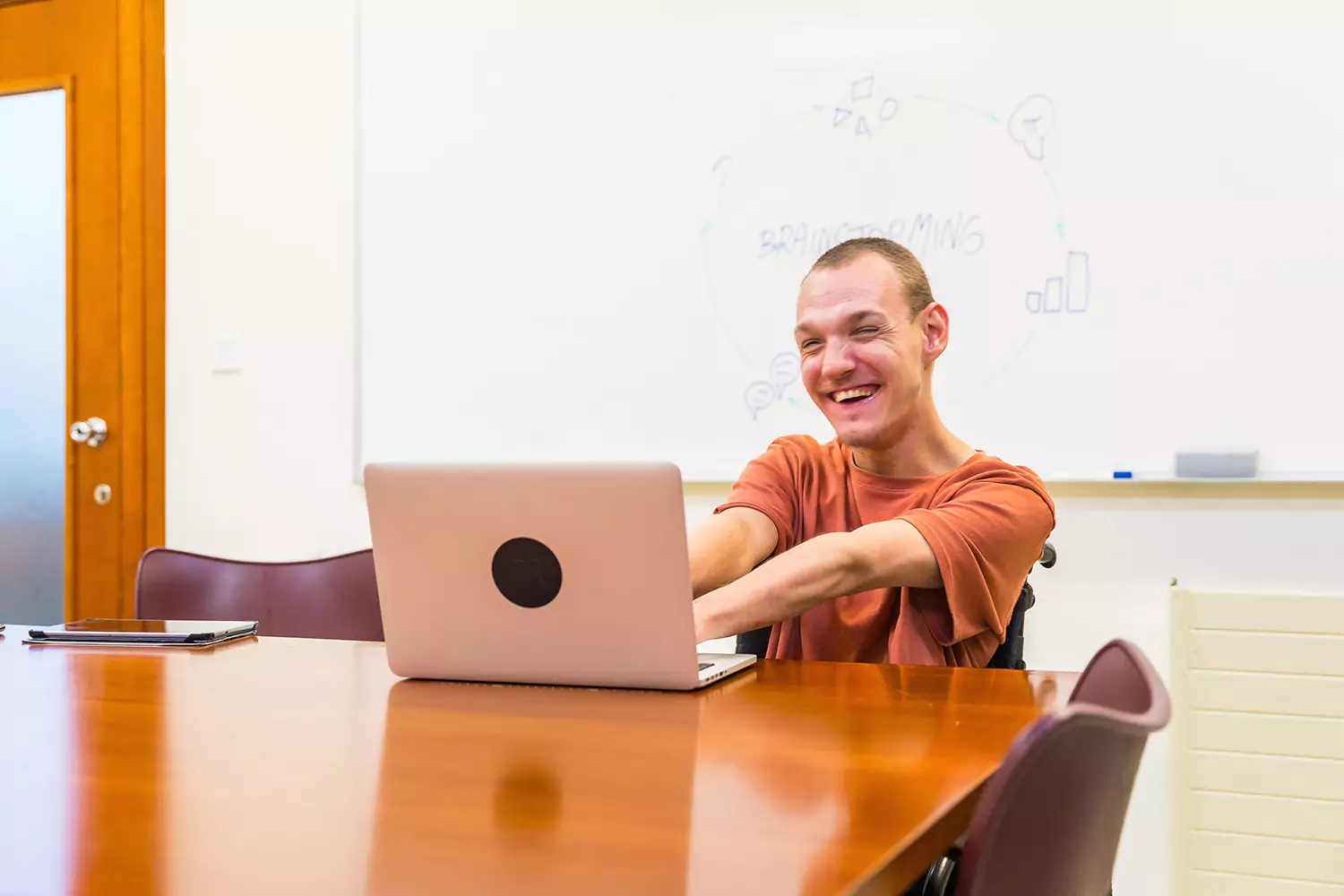 A young man with a disability is using a laptop to learn and complete school tasks