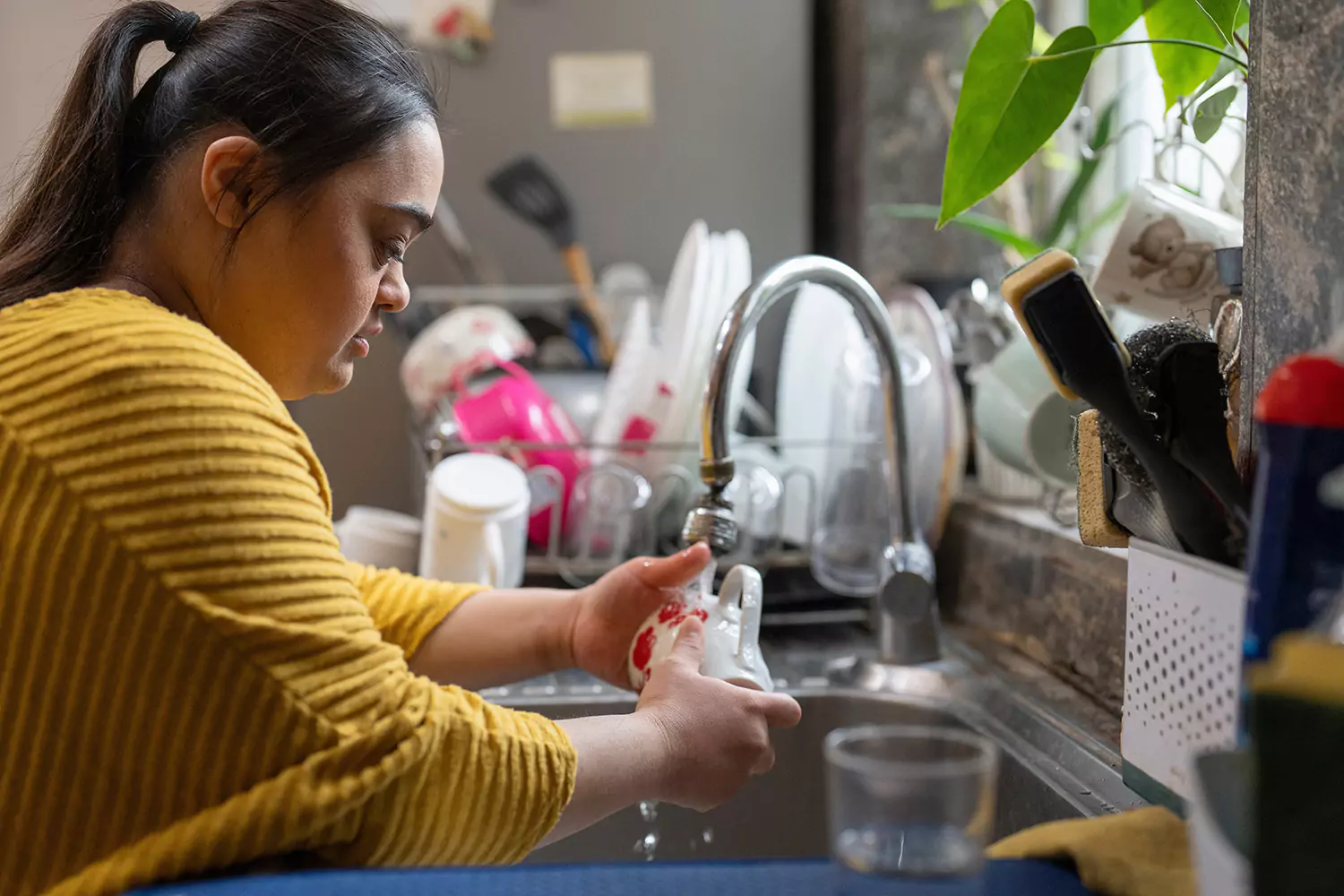 A woman with down syndrome washing dishes in a kitchen