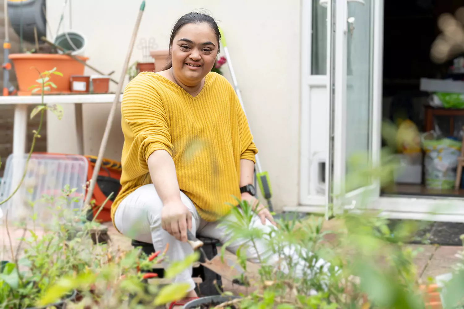 A woman with down syndrome is smiling while sitting in her backyard garden