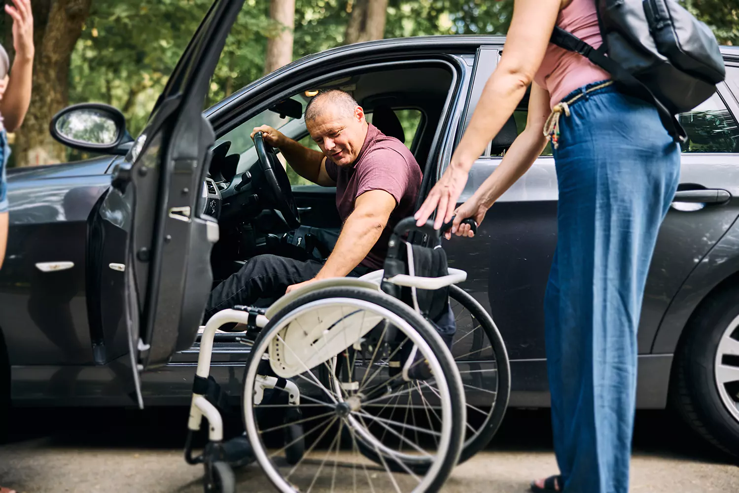 A man with a physical disability is being helped out of a car and into a wheelchair